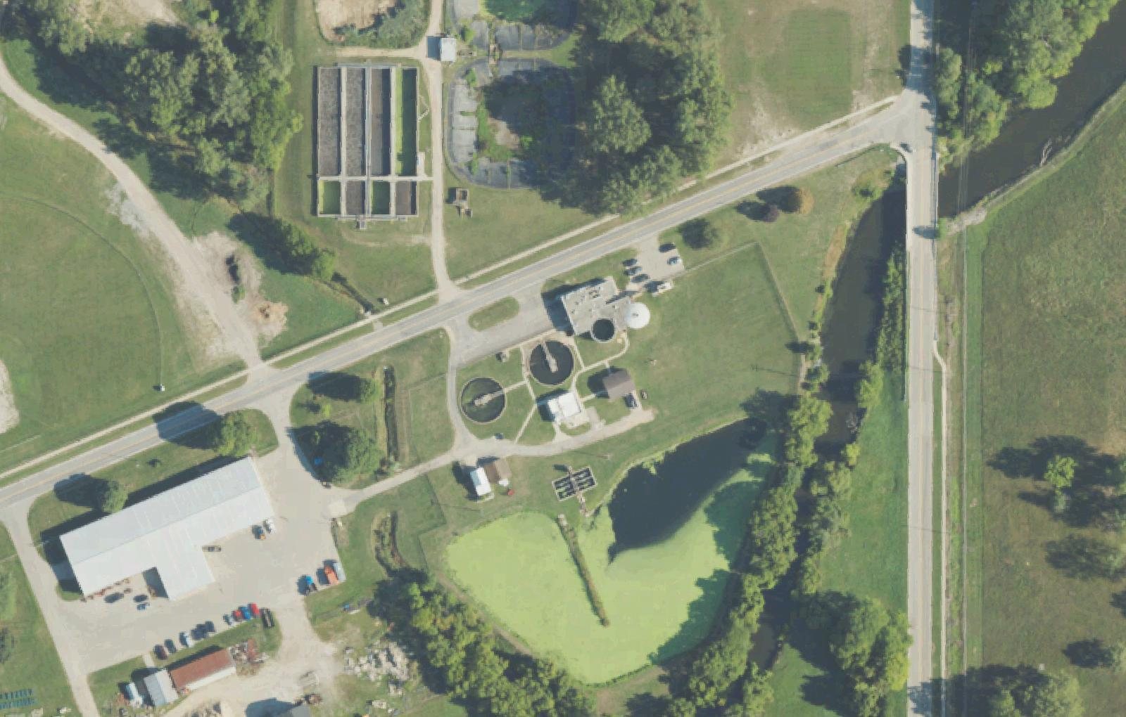 Aerial view of the Alma Wastewater Treatment Plant showing two round clarifiers, aeration basins and a polishing pond beside the Pine River